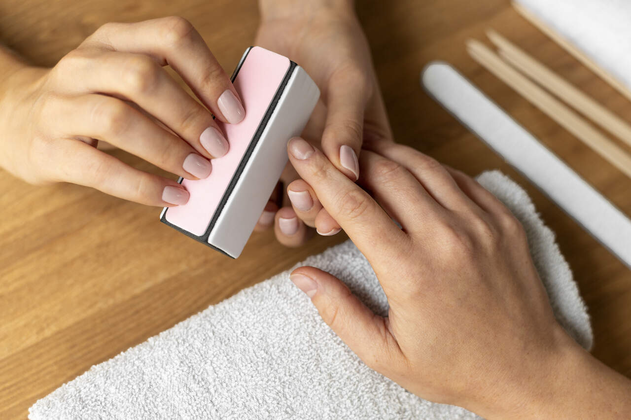 Manicure preparando unhas de cliente para esmalte durar mais tempo
